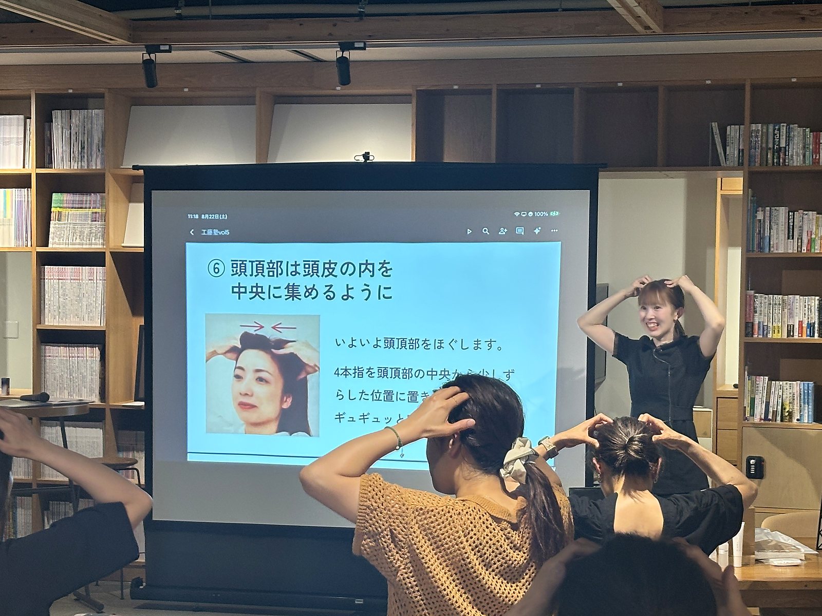 セルフマッサージ講習の様子。講師がスクリーンの前で手の動きを実演している